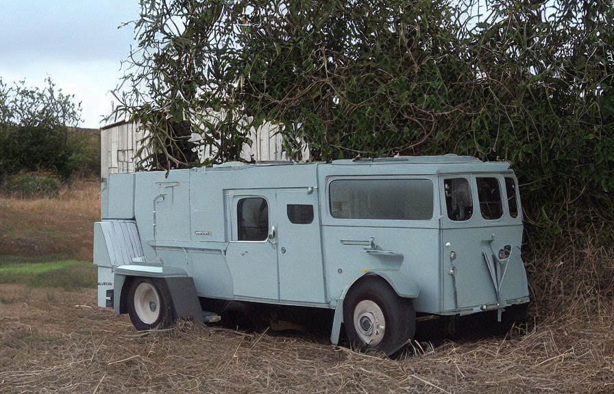 Vintage light blue 6-wheeled armored vehicle parked in front of bush with building in background