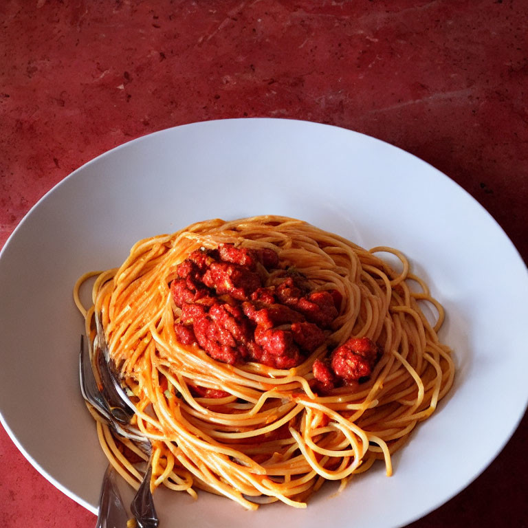 Plate of spaghetti with tomato sauce, meatballs, and fork on red textured surface