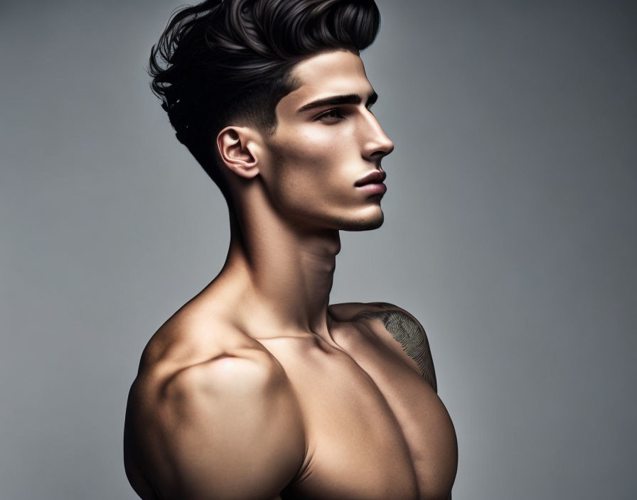 Young man with styled hair and shoulder tattoo on gray background