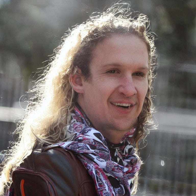 Blond man in leather jacket and scarf smiling outdoors