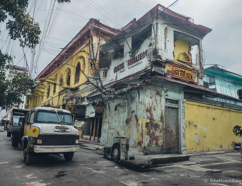 Weathered corner building with peeling paint and parked truck under cloudy sky