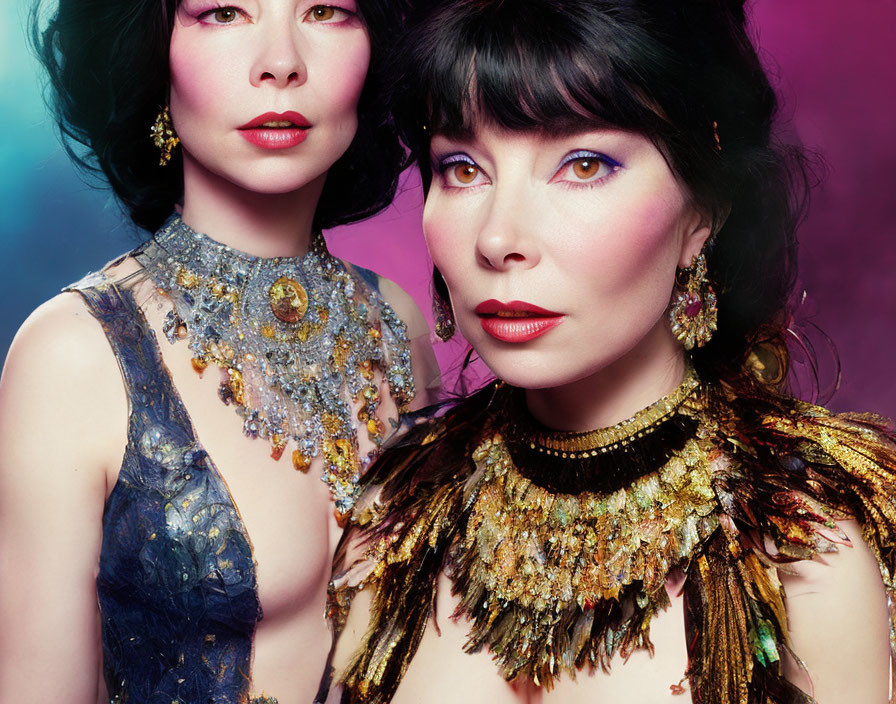 Two women in striking makeup and gemstone-adorned gowns on vibrant background