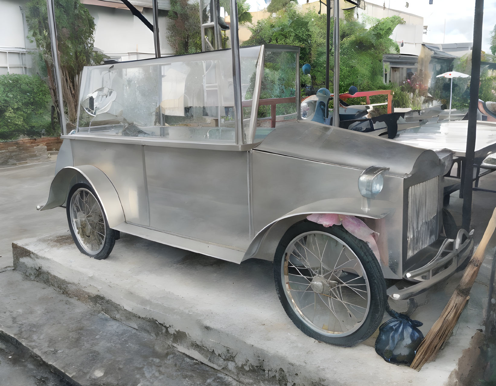 Vintage Silver Car Model Displayed on Concrete Among Plants under Bright Sky