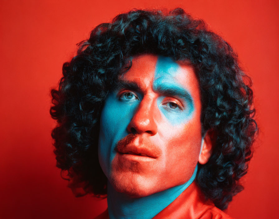 Curly-Haired Man with Half Blue Face on Red Background