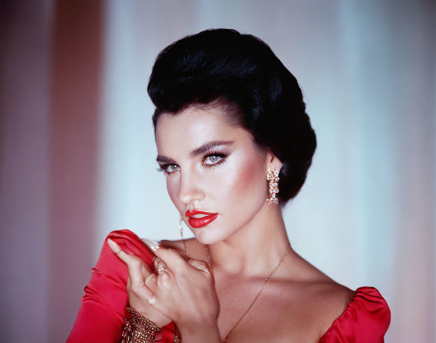 Dark-haired woman in elegant updo, wearing red and gold jewelry, posing gracefully.