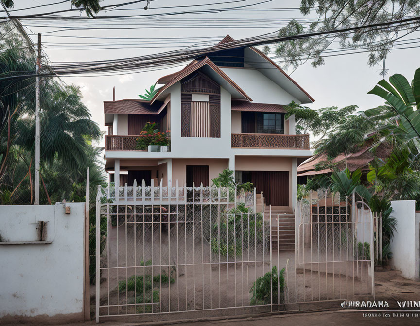 Two-story house with gabled roof, balconies, white railings, surrounded by greenery.