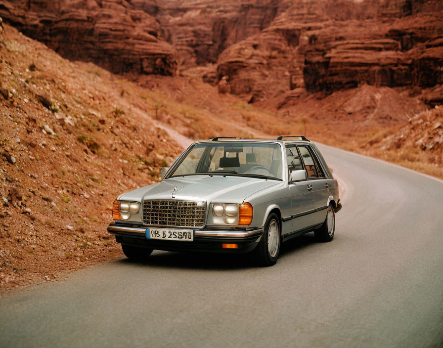 Silver classic car on asphalt road with red canyon walls.