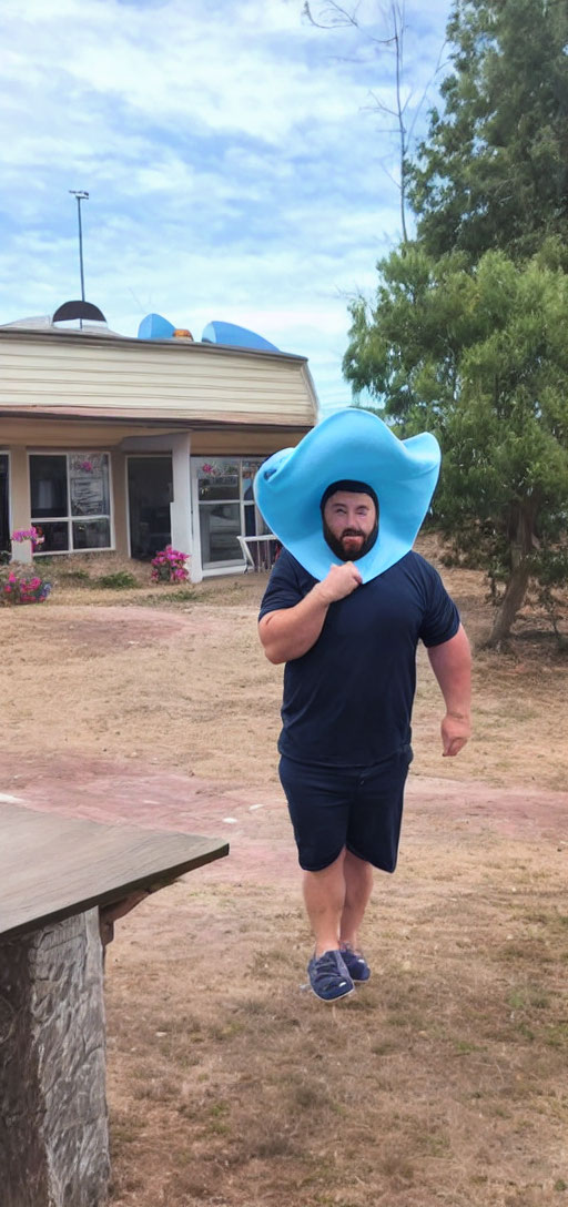 Bearded man in blue outfit and floppy hat walking outdoors