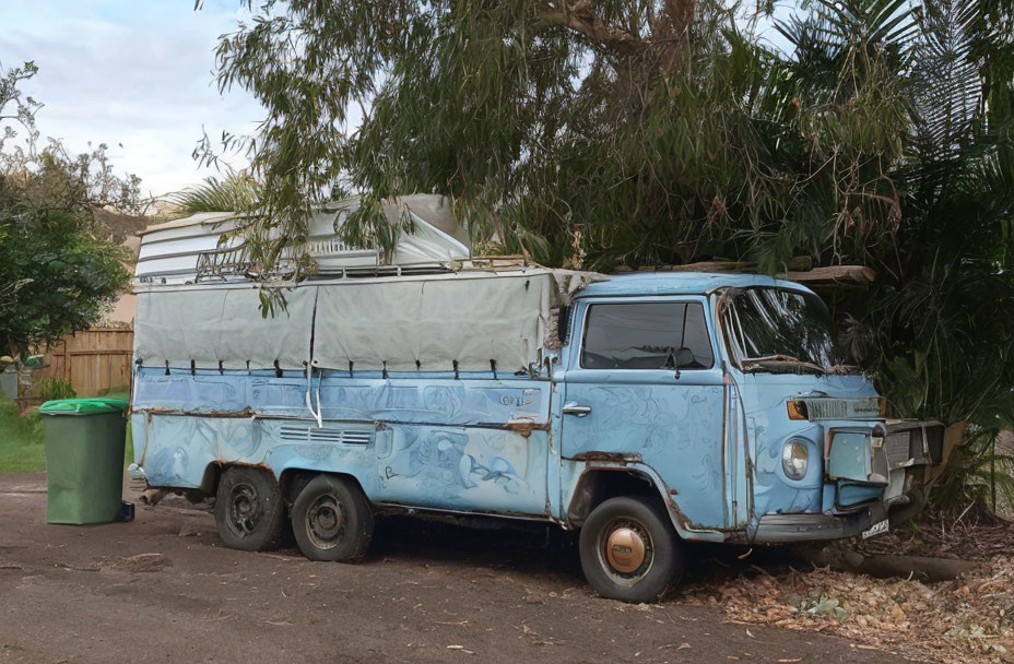 Vintage Blue Camper Van with Pop-Top Roof Parked Near Green Garbage Bin