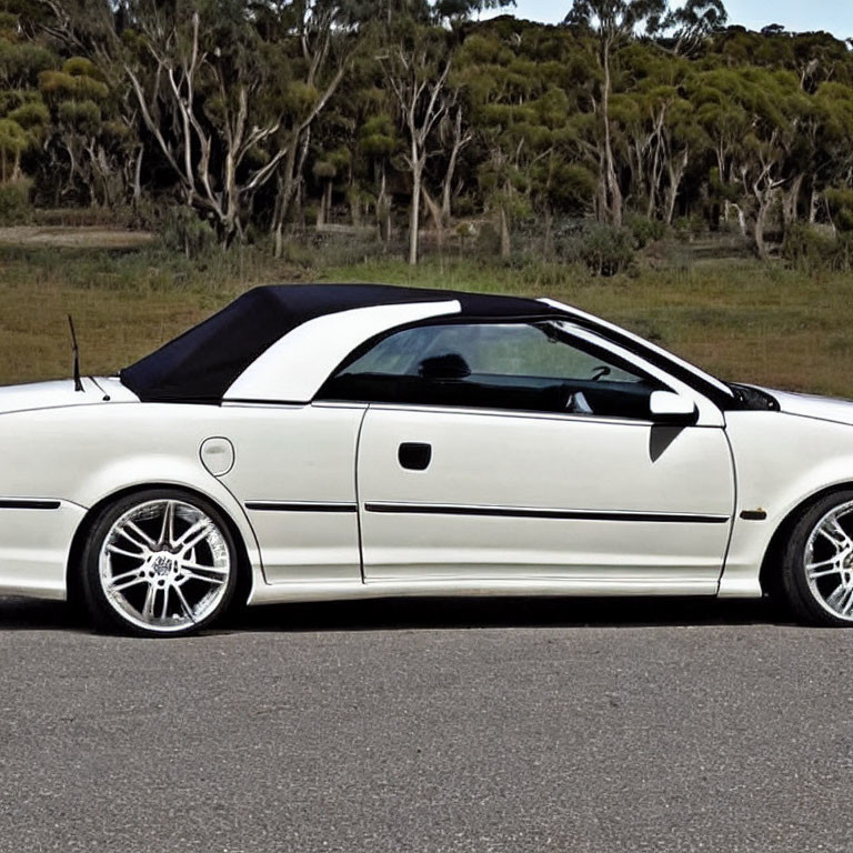 White Convertible Car with Black Soft Top and Aftermarket Wheels Parked by Roadside