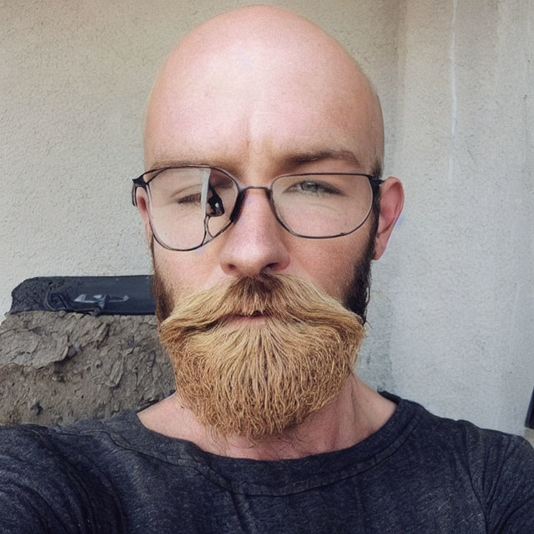 Bald man with twirled mustache in glasses and grey T-shirt