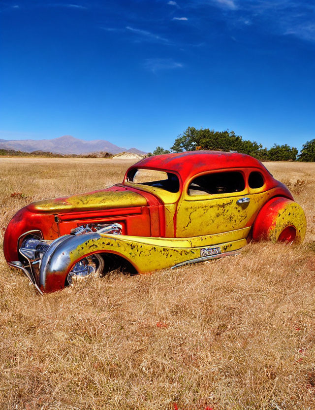 Rusty abandoned car with red and yellow paint in dry field under blue sky