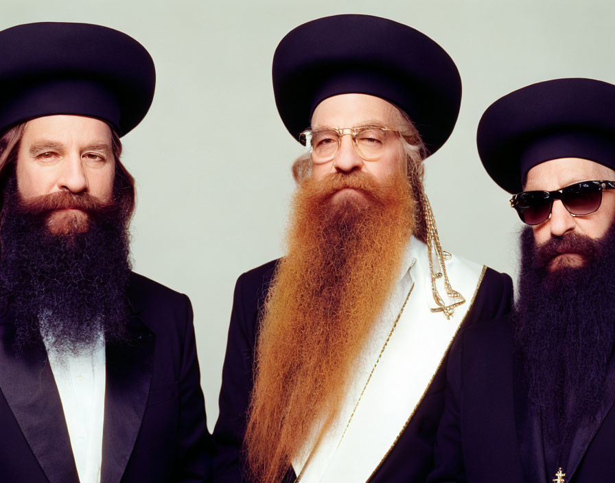 Men with long beards and black hats in religious attire on light background