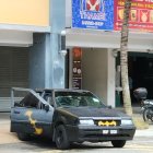 Black sports car parked in front of shop with open garage doors and person inside; colorful banners above