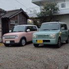 Abandoned cars and buildings with a man standing under cloudy sky