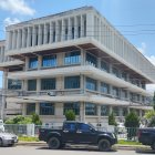 Tiered Brutalist Building with Overhanging Floors and Vintage Cars Under Blue Sky