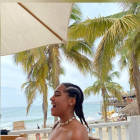 Profile view of person with dark hair against sunny sky, sea, and trees