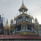 Traditional multi-tiered temple with golden spires and tiered roofs against hazy sky