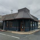 Victorian-style house with dark exterior and ornate trimmings on street corner under cloudy sky