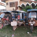 Colorful tuk-tuks with people in helmets on residential street