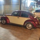 Classic two-toned soft-top car next to water puddle, with vintage station wagon and house in