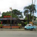 Deserted dusty town street with vintage bus, rustic buildings, and overcast skies.