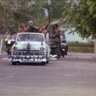 Classic cars and bicycle on tree-lined street from early to mid-20th century