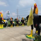 Anthropomorphic bird artwork with chicken heads and human-like legs walking on dirt path