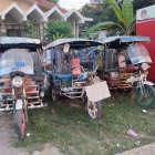 Colorful auto rickshaws parked on residential street with greenery backdrop