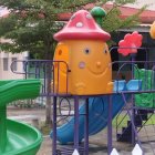 Vibrant yellow and purple playground with slides and climbing holes, green safety flooring, white fences,