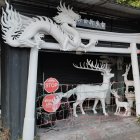 Colorful Dragon Sculpture with Blue Mane Holding Red Orb Under Wooden Archway