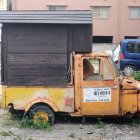 Vintage yellow food truck parked by dusty road with makeshift upper level and train carriage in background