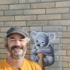 Man with glasses and top knot hairstyle edited with large koala on shoulder against beige background