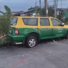 Green and Yellow Taxi with Tree Branch Stuck in Window on Urban Roadside