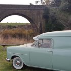 Vintage vehicles and trailers in desert landscape under large bridge