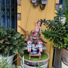 Red-hat garden gnome on tree stump with green plants against yellow wall