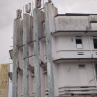 Four-story narrow house with rusted blue façade, balcony, weathervane, vintage car