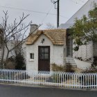 Quaint cottage with thatched roof and flowers, elderly woman by picket fence