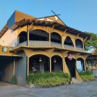 Historic two-story building with arched openings and lush foliage against a clear blue sky