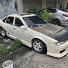 Custom white car with body kit and spoiler parked on urban street.