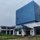 Surreal floating blue cube building with colorful explosive base above abandoned ground structures under scattered papers in the