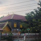 Asian-style Wooden Building with Multi-tiered Roof Amid Lush Greenery and Hot Air Balloons