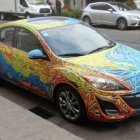 Colorful Patterned Car Parked on Snowy Street with Cars and Trees