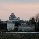 Futuristic dome-shaped building with metallic roof and spires against dusky sky in tree-filled landscape