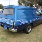 Eclectic vintage blue caravan in pine tree clearing with wildflowers and white bird