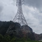 Metal Eiffel Tower-like structure on hilly terrain under cloudy sky