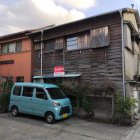 Vintage teal car parked by dilapidated building under cloudy skies