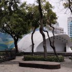 Modern building with arch entrance, leafy trees, curved bench under clear skies