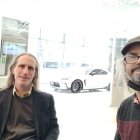 Stylish men in hats and sunglasses in snowy cityscape with sports car