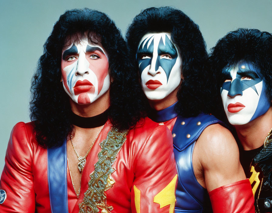 Three individuals in vibrant rock band costumes and elaborate makeup